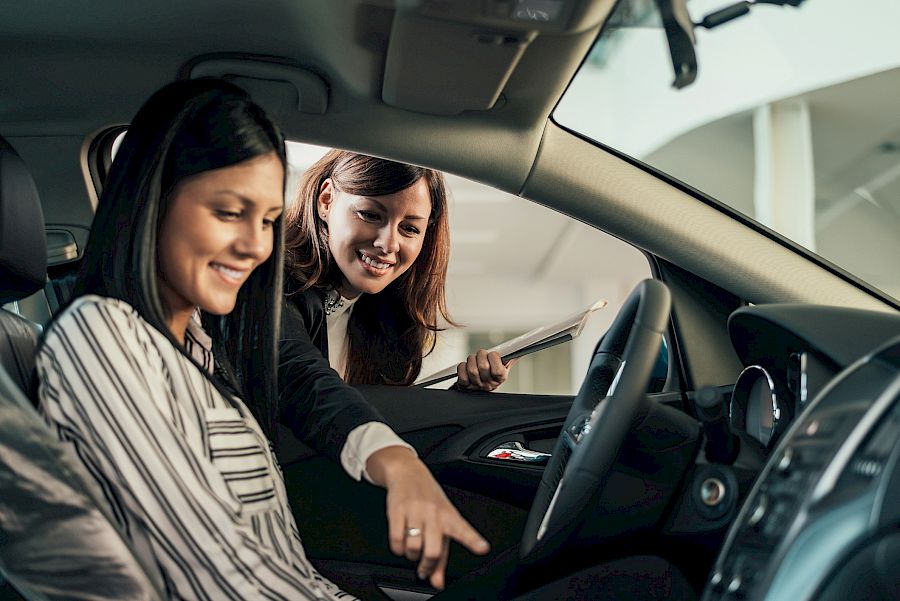 women sat in a new car in the showroom smiling