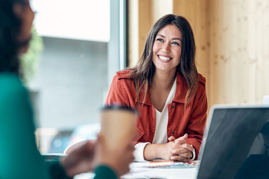 Female professional smiling at laptop talking to colleague