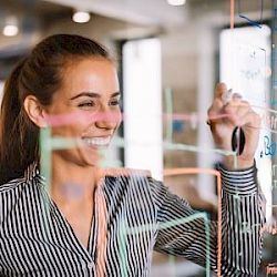 female professional smiling writing on glass project board