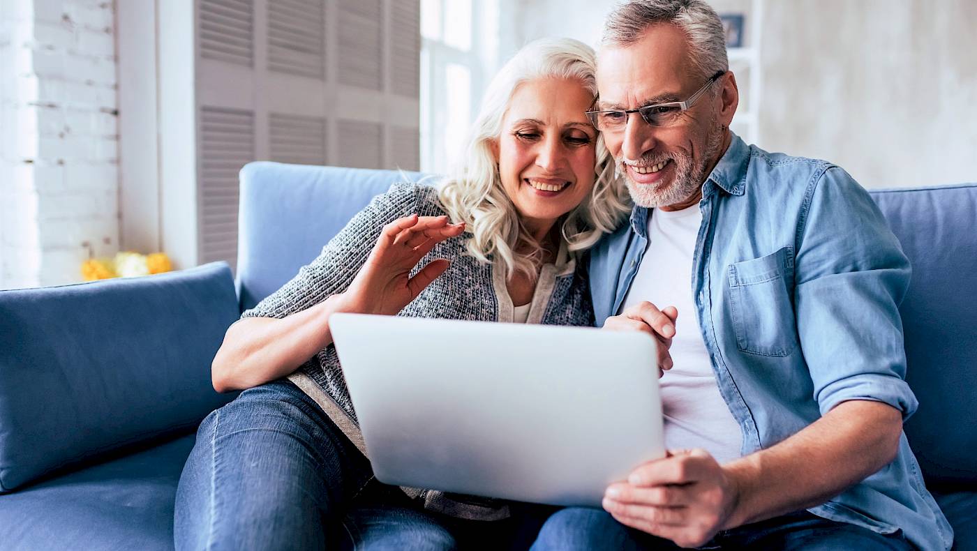 Couple sitting on a sofa, looking at their laptop