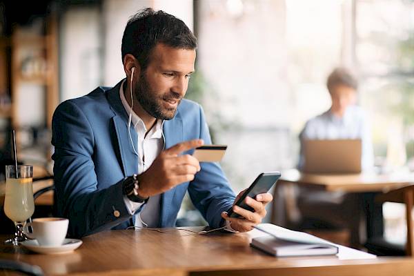 Professional young male in cafe making card payment on mobile phone