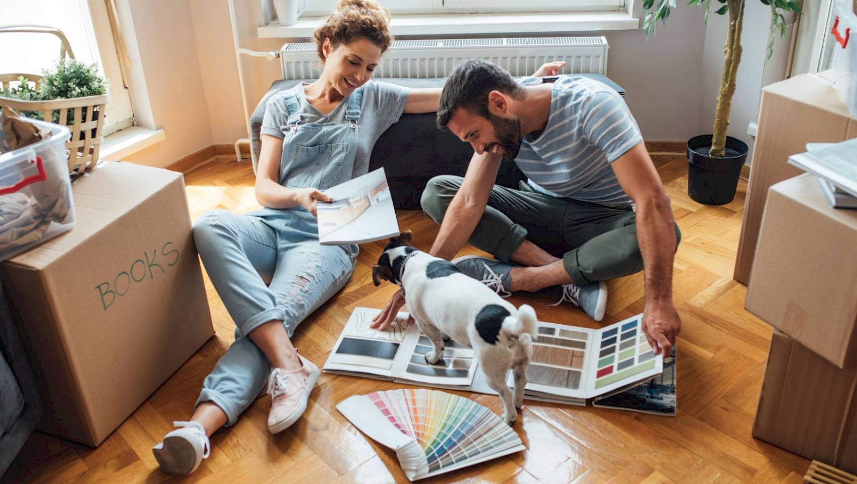 Young couple and dog sitting on floor in new house surrounded by moving boxes