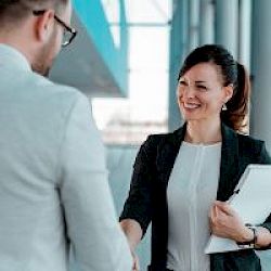 A professional smiling female shaking a man in glasses hand