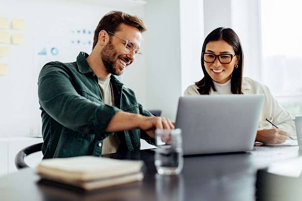 prfoessional male and female looking at laptop screen smiling in office setting