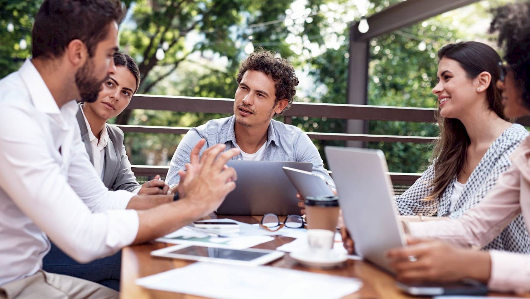 mixed professional team sat at a table outside in a relaxed meeting