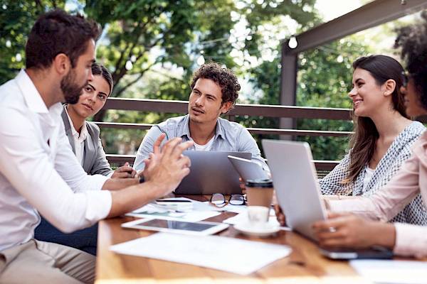 mixed professional team sat at a table outside in a relaxed meeting