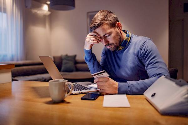 Young worried male looking at bills in front of laptop