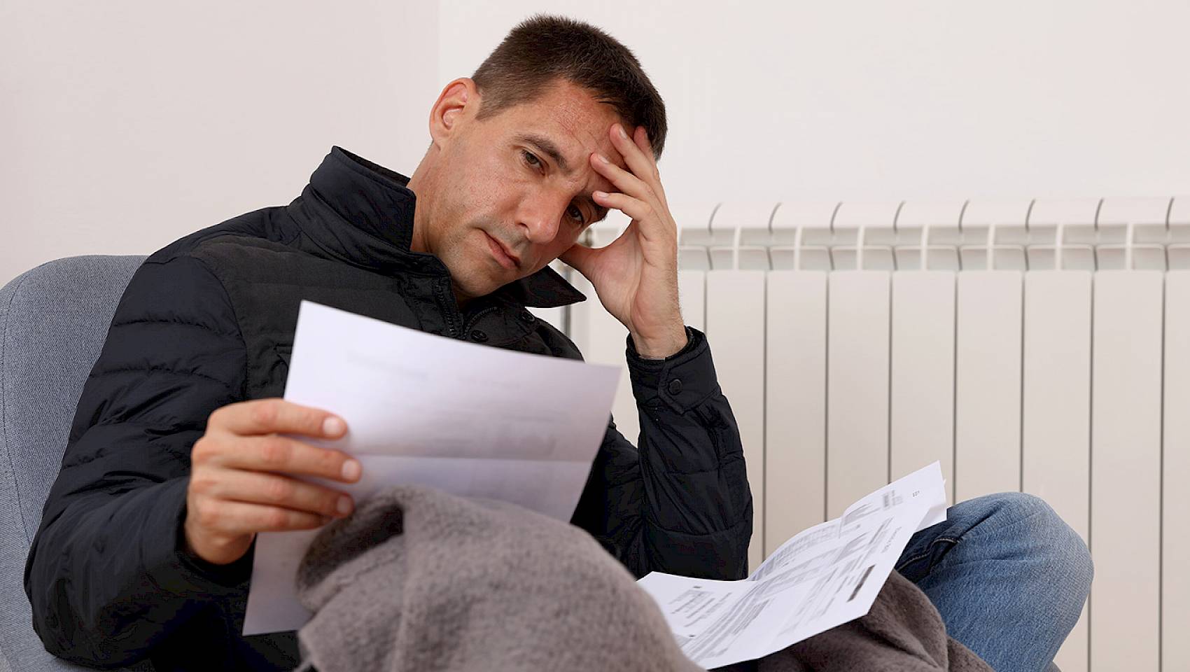 Man looking at bills sat in front of radiator